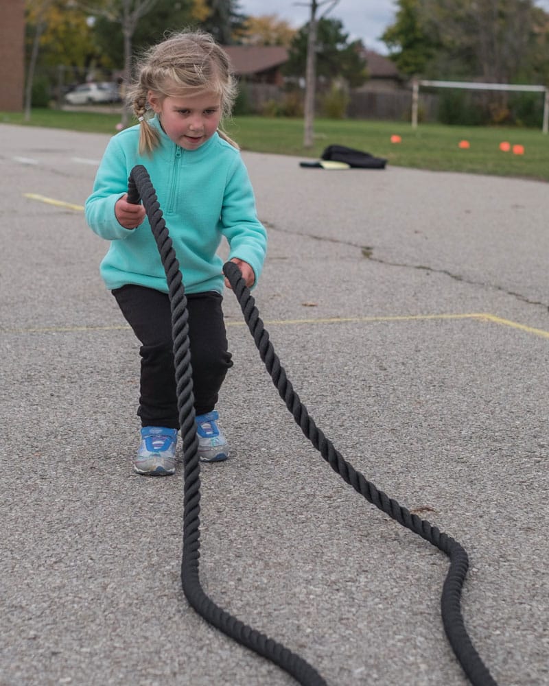 Girl using junior battle rope in school yard