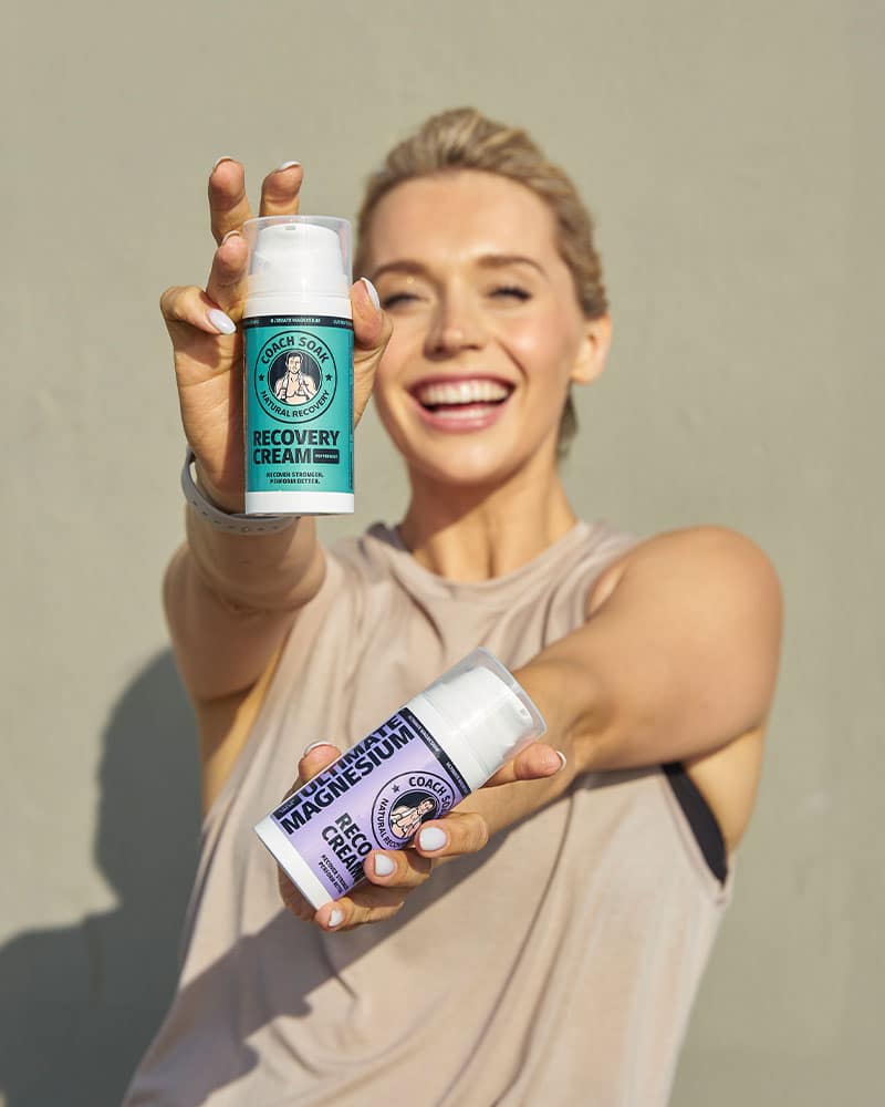 Female holding both scent options of Coach Soak Recovery Cream