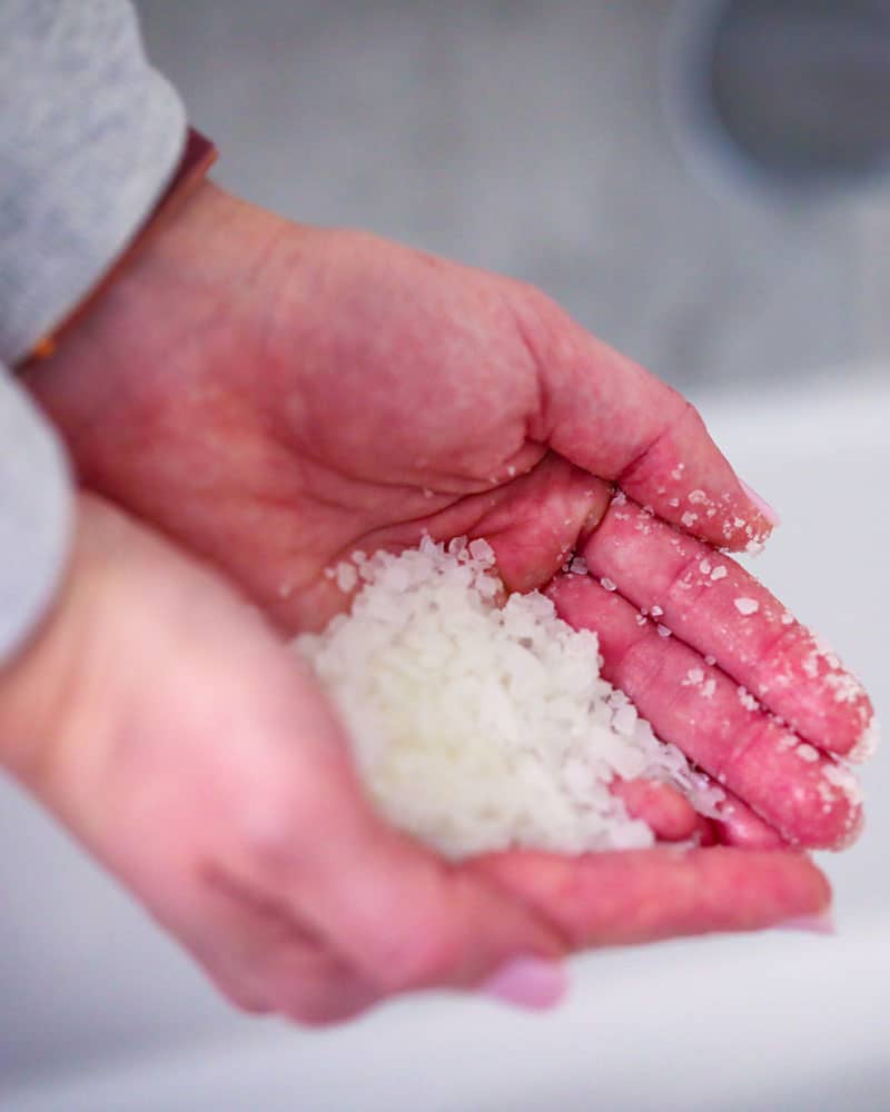 Hands holding a scoop of bath soak by coach soak to put in the bath for muscle recovery