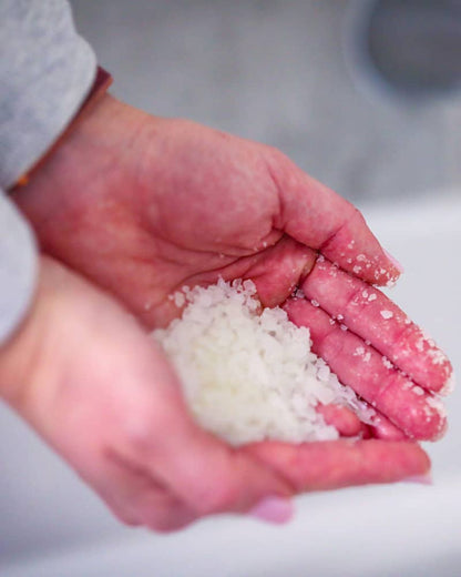 Hands holding a scoop of bath soak by coach soak to put in the bath for muscle recovery