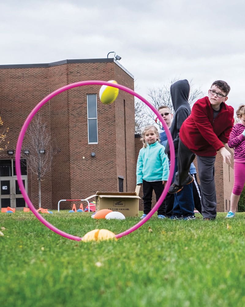 boy throwing football through hoop on base