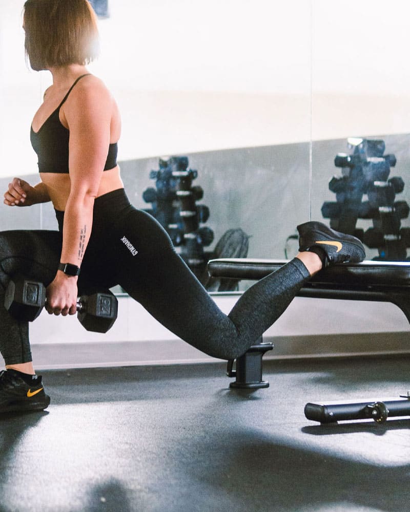 Female athlete in gym using dumbbells with A Frame rack behind her